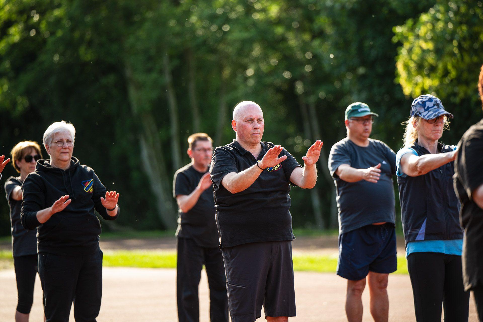 Die Tai-Chi-Chuan-Gruppe des GSV Geldern übt im Freien eine Form mit erhobenen Handflächen